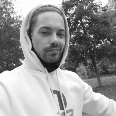 A black and white selfie of a bearded man wearing a white hoodie in an outdoor setting with trees.