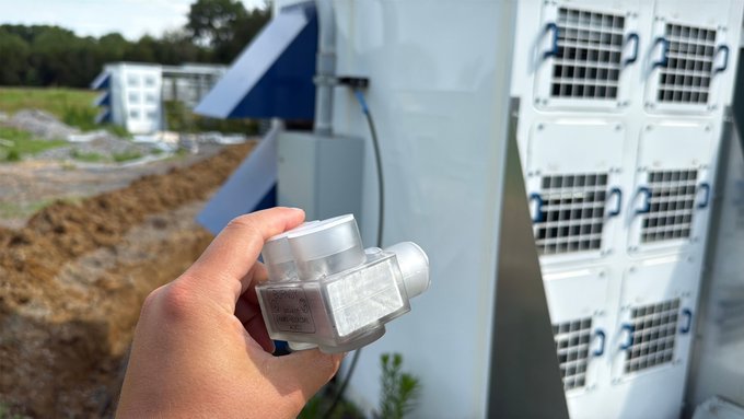 A hand holds a "Burkert" solenoid valve in front of industrial cooling equipment, seemingly unrelated to the playful Bitcoin mining inquiry in the caption.