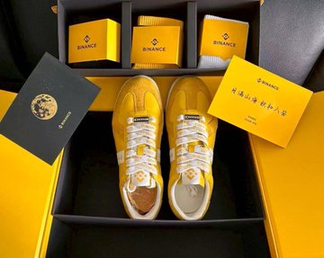 A pair of yellow and white sneakers sits in a black box alongside yellow 'BINANCE' branded socks, a black booklet, and a yellow card with Chinese characters.