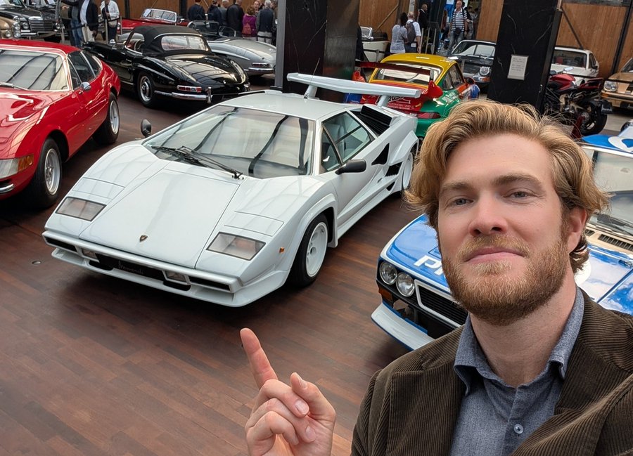 A smiling young man with wavy blonde hair and a beard points excitedly at a white Lamborghini Countach displayed at a classic car museum, surrounded by other vintage sports cars including a red Ferrari and a Porsche.

The post humorously references the Lamborghini's iconic status by pricing it in Bitcoin and "Bluke coins," playing on the idea that such a legendary supercar deserves to be valued in alternative cryptocurrency rather than traditional currency.