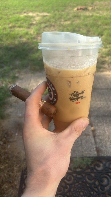 A hand holding a cigar and a clear plastic cup of iced coffee in a branded "Effingut Roasters" cup, photographed outdoors on a patio.