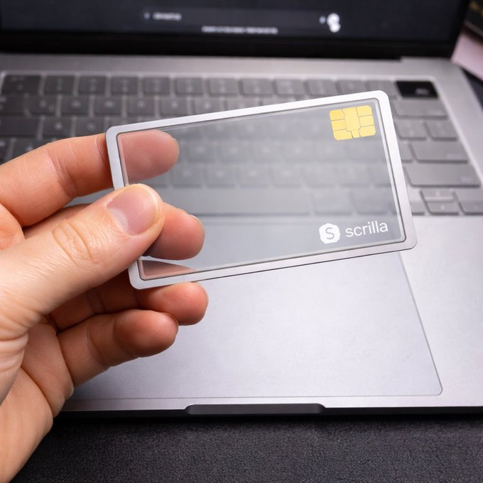 A hand displays a clear plastic card with an embedded chip and "scrilla" branding against the backdrop of a laptop keyboard, exemplifying the post's message that simplicity—not complex hardware setups—is the future of crypto security.