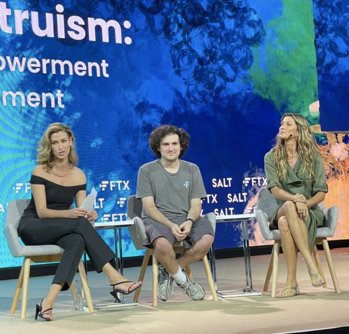 A panel discussion on a stage features three people seated on stools in front of a backdrop with "FTX" and "SALT" logos, including entrepreneur Mark Zuckerberg in the center, with text about "truism," "owerment," and "ment" visible on the screen behind them.