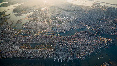 An aerial view shows a densely built coastal city with waterways, a river, bridges, and surrounding hills.
