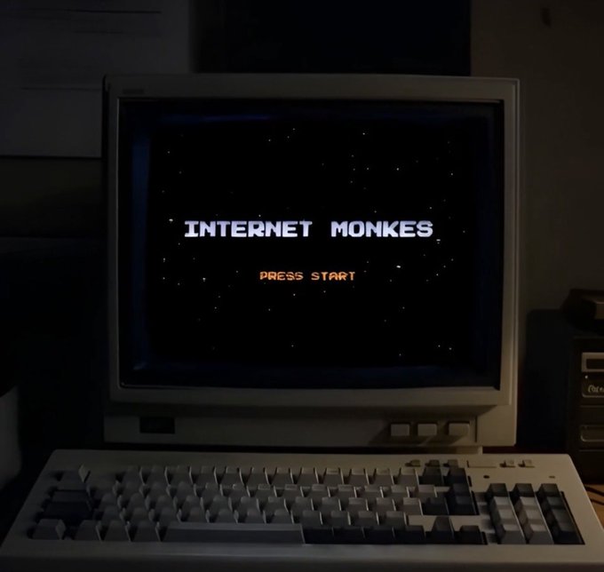 A vintage CRT monitor displays a retro video game title screen reading 'INTERNET MONKES' with 'PRESS START' below it, sitting on top of an old keyboard.