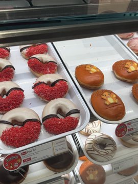A display case at a bakery showing decorated donuts, including red sprinkle donuts and pumpkin-shaped donuts.