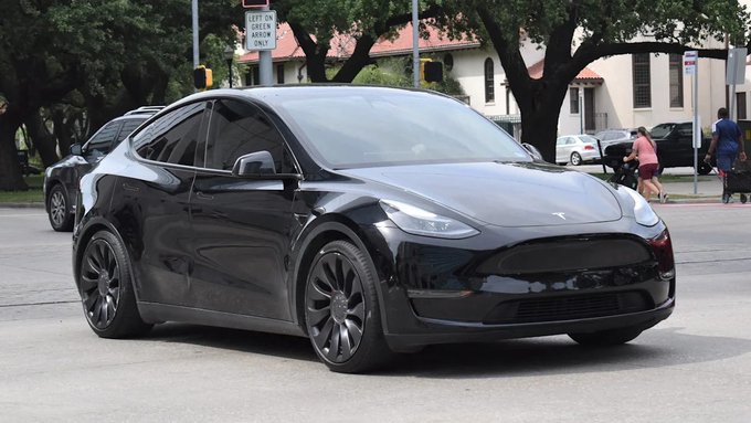 A black Tesla Model Y is parked on a street, fitting the post about selling a Tesla for XRP cryptocurrency. A "Left Turn Green Arrow Only" sign is visible in the background.