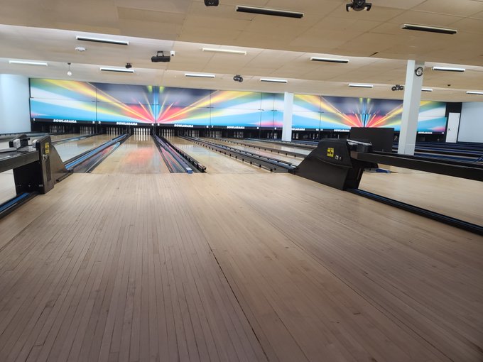 An empty bowling alley featuring multiple lanes, polished wood floors, and colorful neon lights above the pins.