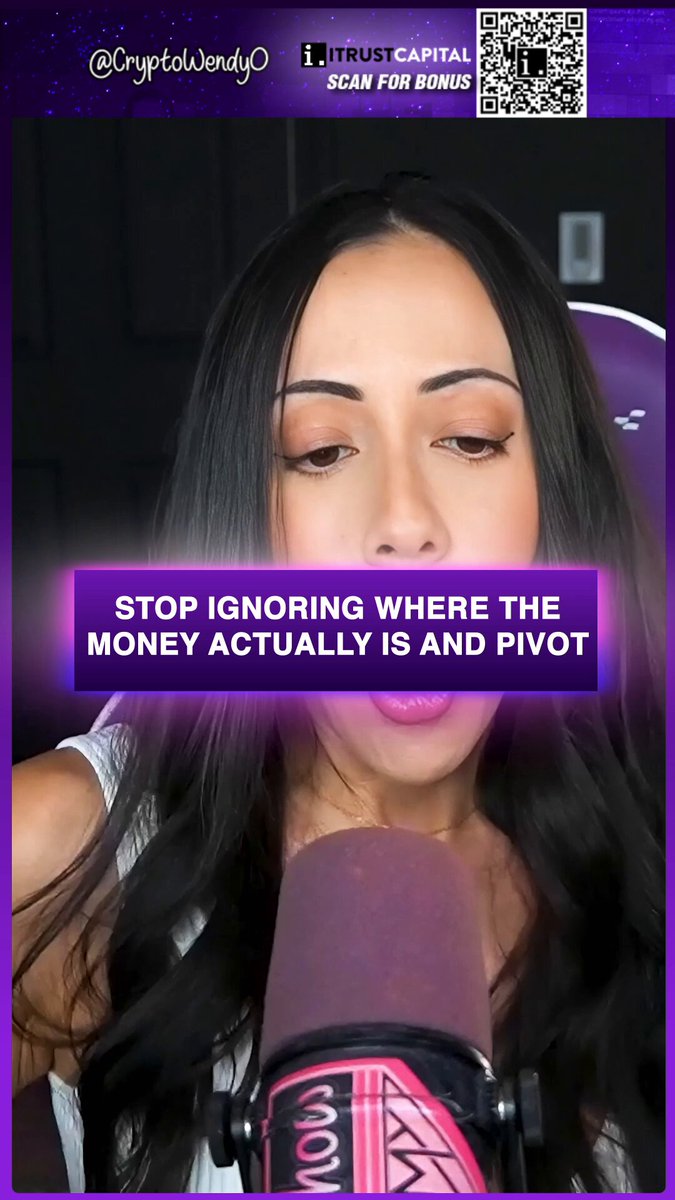 The image shows a woman wearing a microphone stand behind a purple computer monitor screen that has information related to trading in the cryptocurrency market. The text displayed at the top of the screen says "Stop ignoring where the money actually is... pivot there and actively trade." This suggests that the content may be related to cryptocurrency trading, specifically on how to make money through crypto projects or by pivoting with AI and DeFi strategies when it comes to managing digital assets in the stock market.
