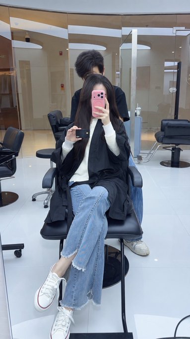 A person wearing a black jacket and ripped jeans takes a mirror selfie with a pink phone while sitting in a salon chair, holding a small black card up to the camera to showcase the newly received MSX black card mentioned in the post.
