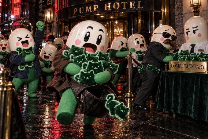 A promotional image for the movie 'Hotel Bitcoin' showing egg-shaped characters with green dollar sign bodies in suits at the entrance of the 'PUMP HOTEL', with a security guard at a 'COMPLIMENTARY' desk.