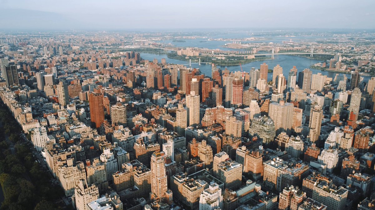 The image shows an aerial view of a city with tall buildings, including skyscrapers and apartment buildings. The city appears to be densely populated, indicating that it could be New York City or another major urban center. The photo has been edited to focus on the cityscape, making it the main subject.