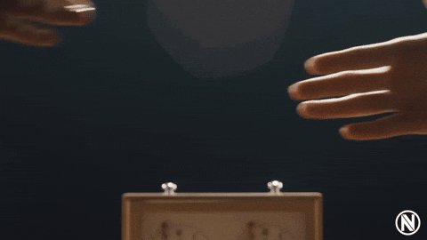The image features a wooden box with two clocks, one of which has its hands pointing upwards while the other remains stationary. The clock with its hands pointing upwards appears to be the center of attention as it seems to be "voting" for something or someone. The person's hands are positioned on either side of the box, suggesting that they might be participating in a game or activity involving the clocks and their positions relative to each other.