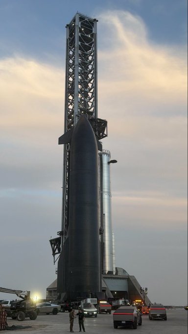 A SpaceX Starship rocket stands tall against a dramatic sky, embodying an unparalleled beauty in its futuristic design and engineering. The image showcases the impressive scale of the rocket and its launch infrastructure.