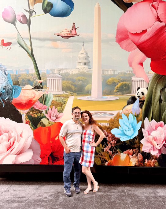 A man and a woman are standing next to each other, posing for a picture in front of a large mural that depicts an aerial view of Washington D.C., with the White House prominently featured. The couple appears to be enjoying their time together as they pose for this memorable moment.