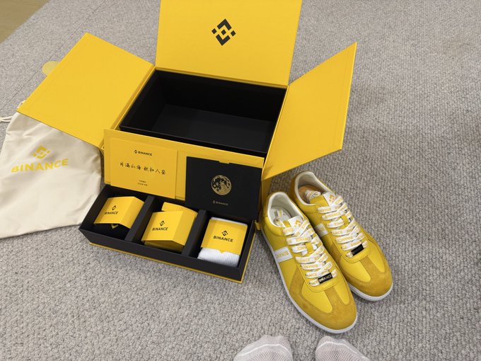A pair of bright yellow Binance-branded sneakers are displayed alongside an open yellow gift box containing Binance-branded cards and accessories, with a Binance dust bag visible on the left, representing the unique Mid-Autumn Festival gift box from Binance mentioned in the post.