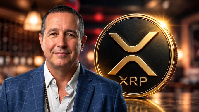 A man in a blue suit standing beside a large gold XRP coin graphic, set against a restaurant/bar background.