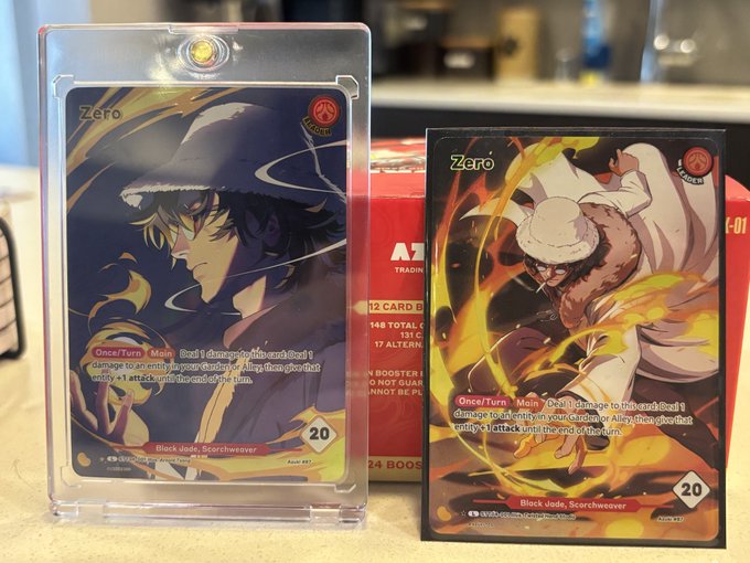 Two "Zero" trading cards from the Azuki TCG are displayed—one in a protective sleeve and one on a red booster box—both labeled "Black Jade, Scorchweaver" with a 20 power rating, celebrating the game's launch day.