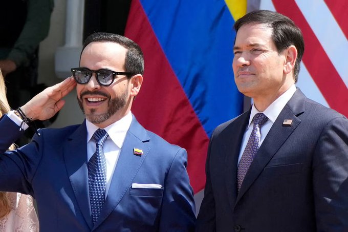 Two men in suits stand before American and Colombian flags, with the man on the left wearing sunglasses and saluting while smiling. The image accompanies a story about Marco Rubio meeting with Colombian President Abelardo De La Espriella to mark a "new era" in U.S.-Colombia relations.