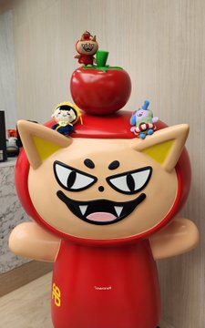 A novelty container shaped like a smiling, mischievous red and tan cat face, topped with small figurines, with Chinese text visible on the base.