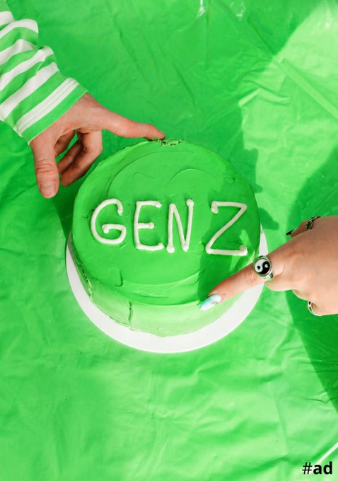 Two hands decorate a green frosted cake with 'GEN Z' written in white icing, set against a bright green backdrop with '#ad' in the corner.
