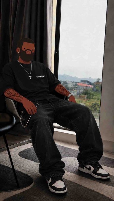 A person sits in a chair by a window wearing a black Represent t-shirt, dark jeans, and black and white sneakers, with a cartoon beard/face emoji overlaid on their face.