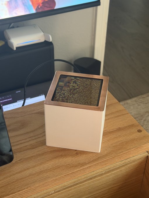 A small white cube-shaped Bitcoin node/miner with a copper-colored top sits on a wooden desk, its display showing what appears to be a hash pattern. The compact device, shown beside a monitor and laptop, represents the modest 500 GH/s contribution to the BIP-110 chain mentioned in the post, embodying the user's commitment to principle over profitability.