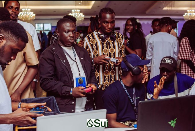 A group of people at what appears to be a gaming or tech event, with some holding controllers; "Sui" and Razer logos are visible.