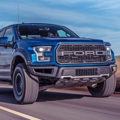 A blue Ford F-150 Raptor truck shown from a front-three-quarter angle with prominent 'FORD' grille lettering.