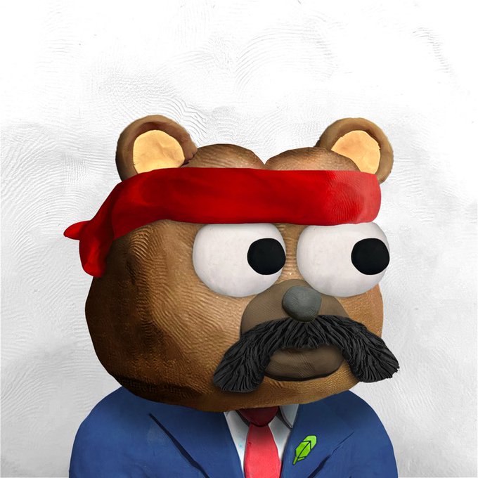 A 3D-rendered brown teddy bear character with a red headband, large googly eyes, and a black mustache, wearing a blue suit jacket, red tie, and a green gem pin.