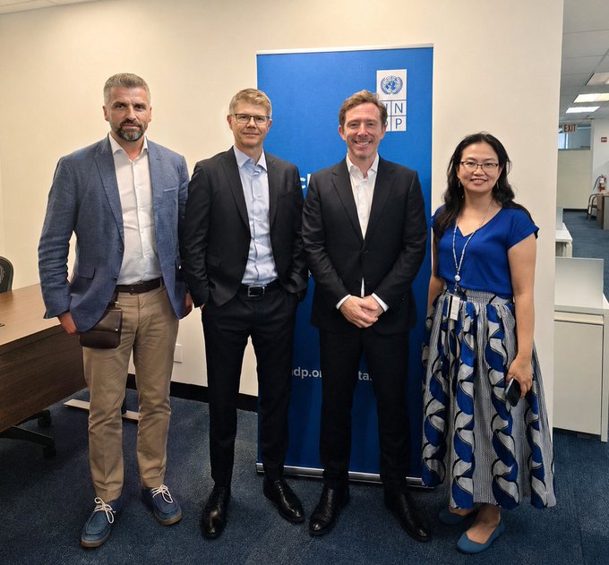 Four professionals pose in front of a United Nations Development Programme (UNDP) banner, marking a partnership between UNDP and the DFINITY Foundation to advance public-sector AI infrastructure on the ICP blockchain across five countries in Latin America, Africa, and Asia, promoting independence from centralized hyperscalers.