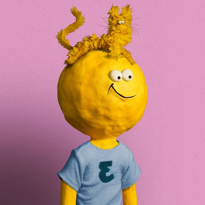A yellow claymation-style figure with a simple smiley face wearing a blue t-shirt with a black 'E', has a fuzzy orange cat-like creature resting on its head against a solid pink background.