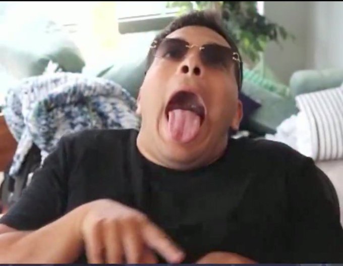A person wearing sunglasses and a black shirt sticks their tongue out at the camera.