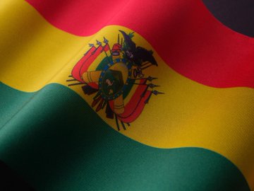The image shows the flag of Bolivia, featuring its distinctive red, yellow, and green horizontal stripes with the national coat of arms at the center, depicted with a rippling fabric effect. This relates to the post as it visually represents Bolivia, the country considering integrating USDT into its national payments system following a significant surge in crypto adoption.
