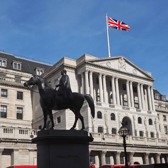 A bronze equestrian statue in front of the Bank of England building in London, with the British Union Jack flag flying above the neoclassical structure.