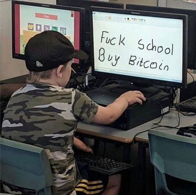 A young child wearing a camo shirt and a backwards cap sits at a computer with a monitor displaying the handwritten-style text 'Fuck School Buy Bitcoin.'