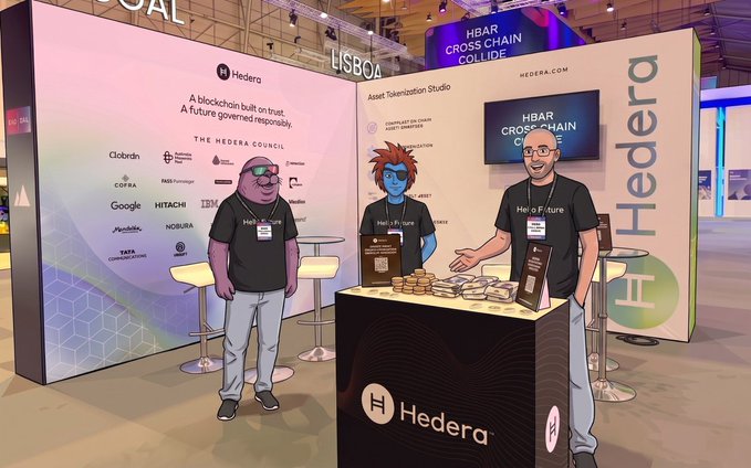 The image features three men standing next to a booth at an event, with one of them wearing a black shirt that says "hedera" on it. The booth has a sign for "Hedera" written on it, indicating its purpose or affiliation. The other two men are dressed in t-shirts and appear to be promoting the event or product related to the "hedera" brand.