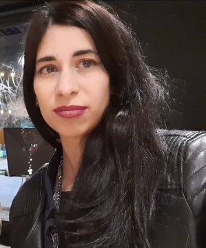 A close-up portrait of a woman with long dark hair, wearing red lipstick and a black leather jacket, with a softly lit background.