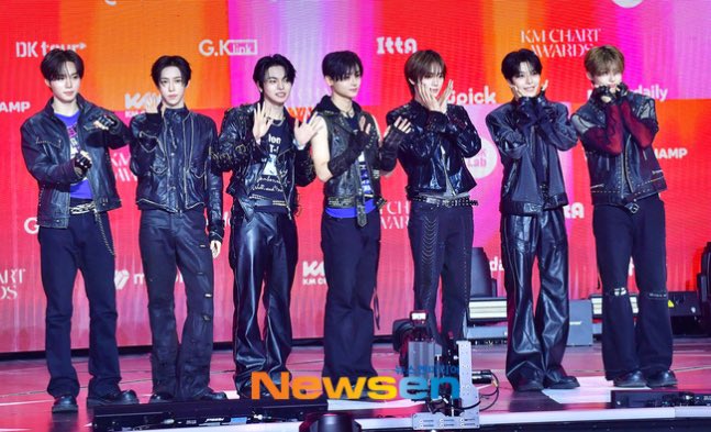 The image shows seven members of the K-pop group BOYNEXTDOOR dressed in coordinated all-black leather outfits at the KM Chart Awards (KMA), with the group's name "WLD1" (referring to their comeback) being celebrated through their unified, edgy styling on stage. The backdrop displays "KMA CHART AWARDS" and various sponsor logos including DK Pocket, G-Knock, and Itta, confirming the awards show setting.