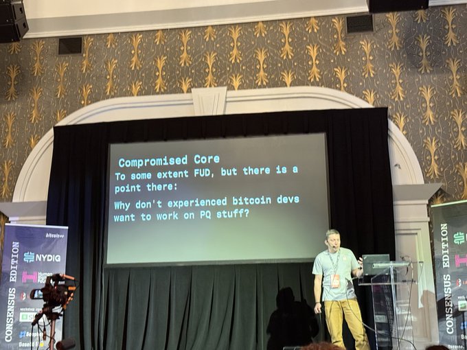 A presenter on stage at a Consensus Edition conference discussing 'Compromised Core' and post-quantum (PQ) stuff for bitcoin.