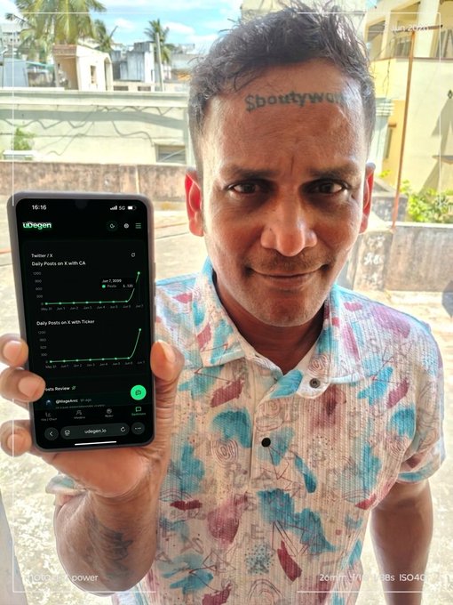 The image shows an older man with facial hair standing next to his phone, holding it up for all to see. His face has a tattoo of "BOUTYWORK" on one side and he also has "typo" written across his forehead in what appears to be black ink. The caption below the image reads: "From Typo to Thousands: The Wildest Story on Solana Today @Arivulife went viral after tattooing a ticker onto his forehead, except he made a typo, accidentally inking $BOUTYWORK instead of $BOUNTYWORK".
