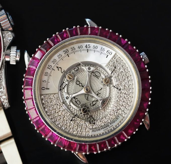 A close-up of a luxury Audemars Piguet watch featuring a diamond-encrusted face, an exposed tourbillon mechanism, and a bezel set with pink/red gemstones.