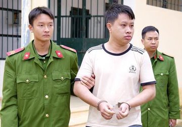 A man in a white shirt with handcuffs is being escorted by two police officers in green uniforms.