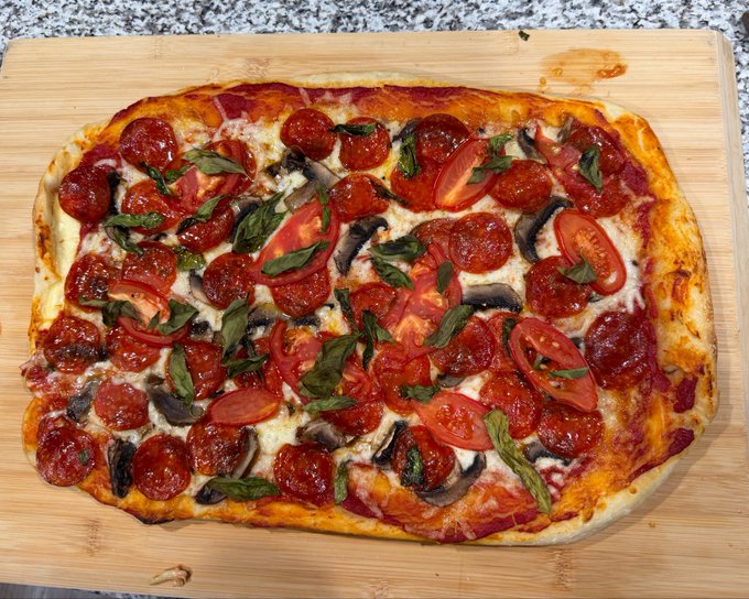 A rectangular homemade stuffed-crust pizza topped with pepperoni, fresh tomato slices, basil, mushrooms, and melted cheese rests on a wooden cutting board. The image visually matches the post's description of a handcrafted pizza featuring handmade dough, garden tomato, basil, and a garlic butter–brushed crust, though the playful "bears are dumb" and "we're going so much higher" remarks have no visual connection to the dish itself.