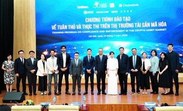 A group photo from a conference shows attendees standing on a stage before a banner reading 'CHƯƠNG TRÌNH ĐÀO TẠO VỀ TUÂN THỦ VÀ THỰC THI TRÊN THỊ TRƯỜNG TÀI SẢN MÃ HÓA' (Training program on compliance and enforcement in the crypto asset market), dated 'Hà Nội, ngày 22 tháng 11 năm 2024'.