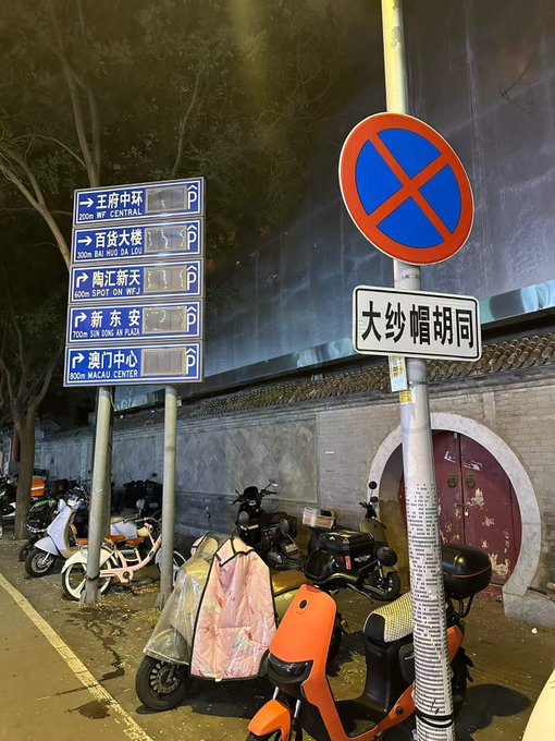 A nighttime street scene in Beijing shows directional signs pointing to landmarks like "王府井中环" (500m WF CENTRAL) and "新东安" (700m SIN XONG AN PLAZA), alongside a "No Stopping" sign and "大纱帽胡同" street sign, with parked scooters and bicycles lining the sidewalk beneath the glow of streetlights. The image perfectly captures the quiet, homeward-bound mood of the post—after navigating the busy web3 world, the traveler has finally returned to this familiar, unassuming hutong alley.
