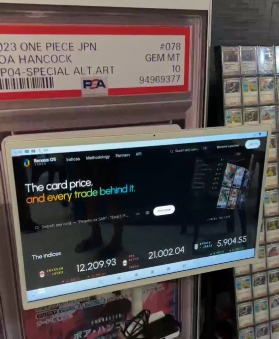 A retail display showing a PSA-graded '2023 ONE PIECE JPN. BOA HANCOCK' card labeled 'GEM MT 10' with barcode 94969377, alongside a screen displaying pricing indexes (12,209.93, 21,002.04, 5,904.55).