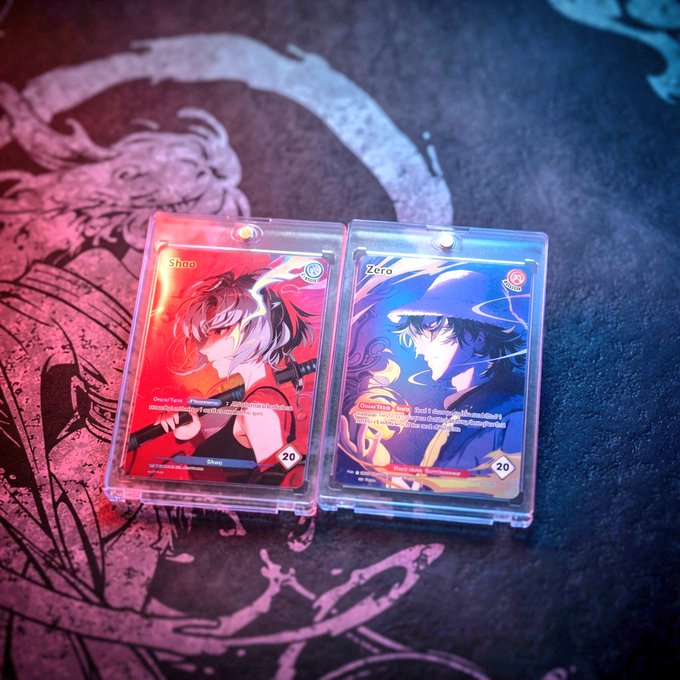 Two anime-style trading cards named 'Shoo' and 'Zero' displayed in protective cases on a dark surface with an illustrated design; each card shows a character and a '20' in the bottom right corner.