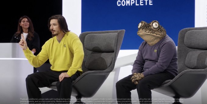 A surreal composite image showing a man in a yellow sweater and a frog-headed humanoid in a purple sweater sitting in grey chairs on a panel show stage, with a woman seated behind them and the word "COMPLETE" visible in the background.