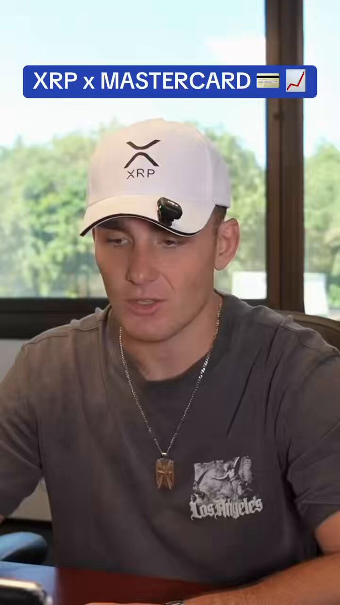 The image shows a man wearing a white baseball cap with an XRP logo, sitting at a desk or table while looking down at his cell phone. The caption of the image reads "People don't understand how big the XRPL x Mastercard partnership is going to be... Massive for $XRP Full video: youtu.be/789OeLg2mJU?". This suggests that there might be a discussion or event related to the XRPL and Mastercard partnership, possibly involving the value of XRP in relation to Mastercard's partnership.